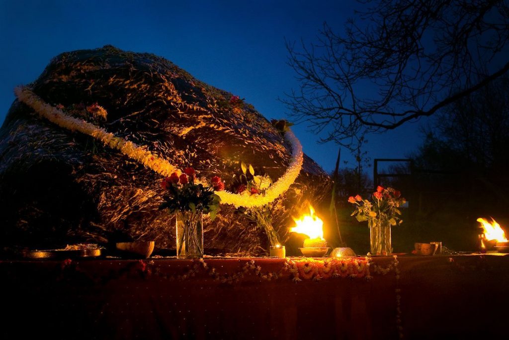 An large shaligram or lingam with flower garland and aarthi at night time in Skanda Vale Monastery UK