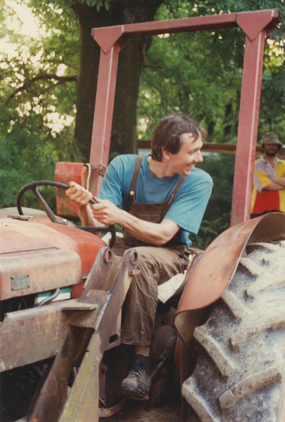 Swami Suryananda in farm clothes, driving a tractor, smiling