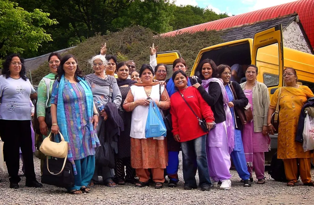 A coach group of Hindu pilgrims smile for the camera by a yellow minibus at Skanda Vale Ashram