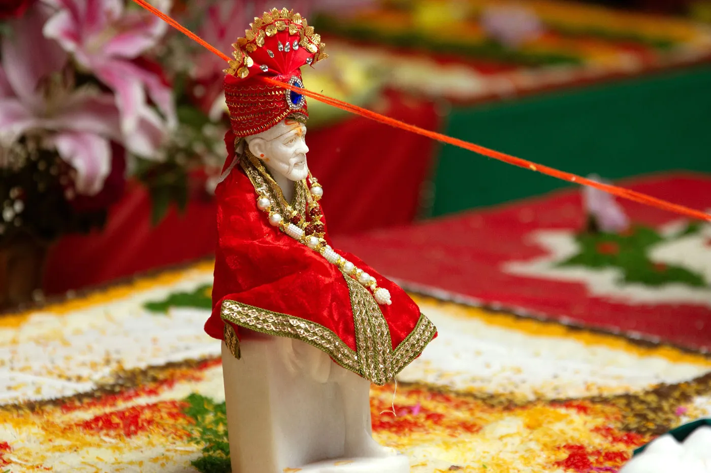A small white marble statue of Shirdi Sai dressed in red