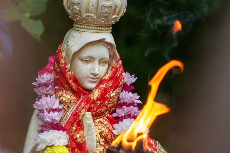 A statue of Mother Mary with flower garland and flame